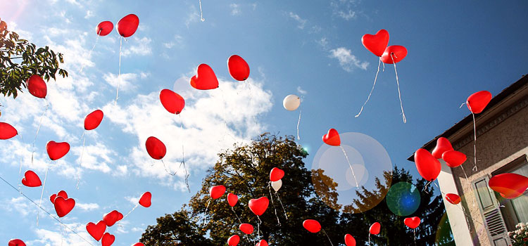 Rote Luftballons in Herzform steigen in den blauen Himmel.